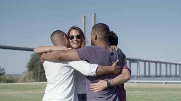 Happy Four Friends Hugging While Standing on Meadow alt