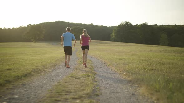 Following Couple Jogging in Dry Grassland in Summer