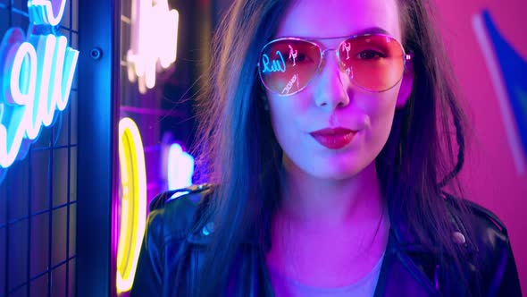 Mixed Raced Woman with Dreadlocks and Glasses Posing Near Glowing Neon Wall in the Dark alt