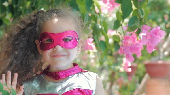Beautiful Llittle Girl in the Superhero Costume, Dressed in a Pink Cloak and the Mask of the Hero alt