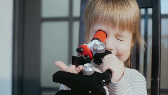 Funny Toddler Holding Toy Microscope in Hands Squinting and Looking Into Microscope with One Eye