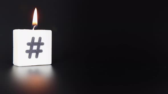 A square candle printed with a hash tag being lit and blown out on a black dark background alt
