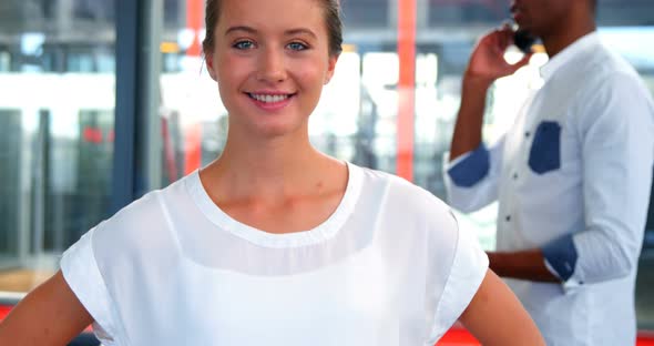 Female business executive smiling at camera while colleague talking on mobile phone alt