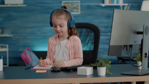 Young Child Wearing Headphones and Drawing on Textbook alt