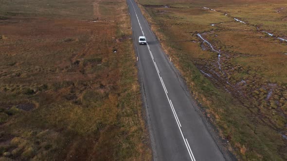 Car travels through tundra terrain landscape during dusk, aerial alt