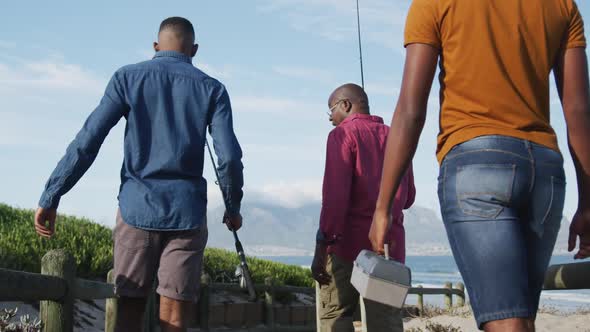 African american senior father and two teenage sons standing on a beach fishing and talking alt
