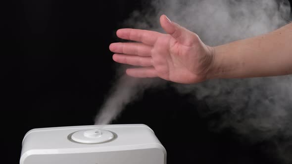 Man holds hand over steam from the air humidifier, free space. Ultrasonic technology