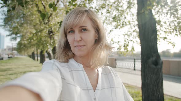 POV Portrait of Cheerful Blonde Posing Outdoors Taking Selfie and Smiling Against Urban Background alt