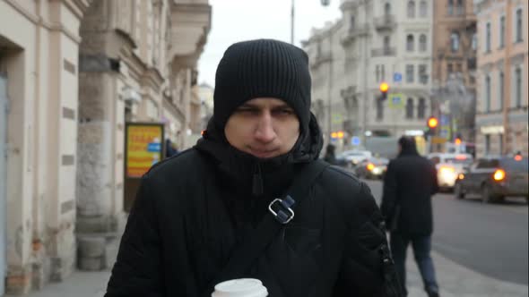 Front View  Of  Young Man Walking Down The City Street And Drinking Coffee