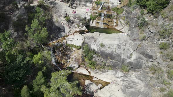 Aerial circular view over people sunbathing on rocks, at waterfall Fecha de Barjas.