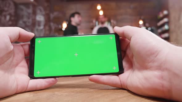 Holding a Phone with a Green Screen in a Busy Cafe alt
