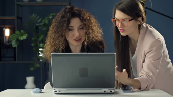 Focused Female Colleagues Sit at Desk in Office Brainstorm Discuss Business Idea Use Laptop