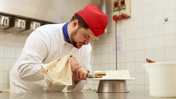 Pastry chef at work in a cake shop preparing and decorating a cake with whipped cream alt