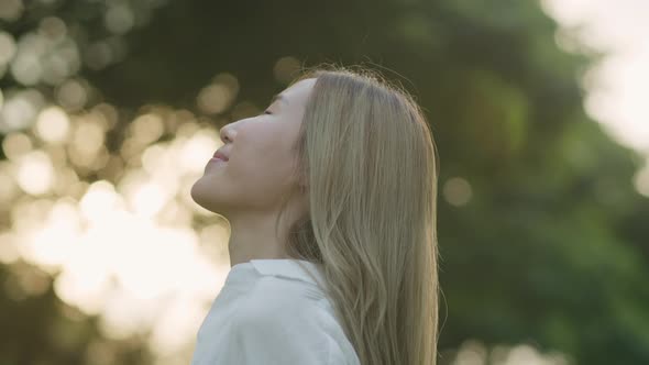 An attractive young Asian female closed her eyes enjoying the breeze in the public park.