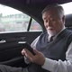 4K Senior businessman sitting on car back seat using mobile phone video conference with partner