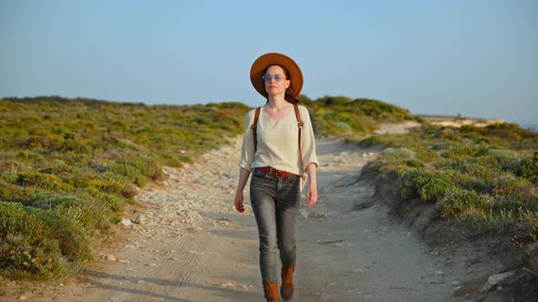 Attractive hiker in a hat walking on a deserted road in the countryside alt