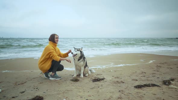 Young Beautiful Female Walking with Siberian Husky Dog on the Beach alt