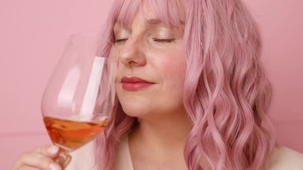Beautiful 20s Woman with Pink Curly Hair Drinking Rose Wine Over Bright Pink Color Background