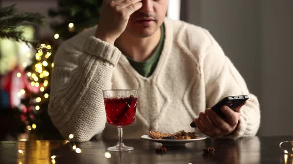 Sad man in white sweater with mobile phone sits on Christmas
