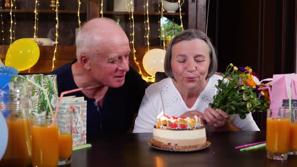 Happy Senior Couple Blowing Candles at Birthday Party