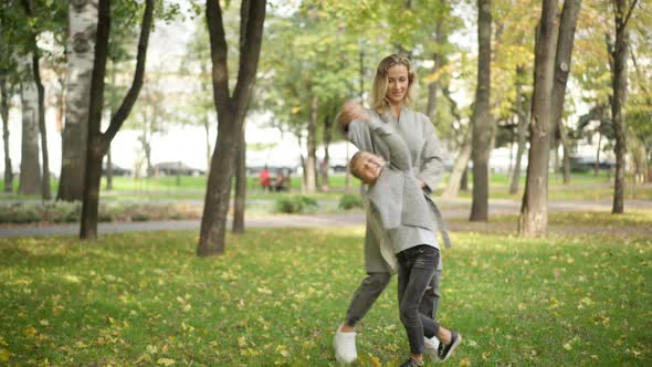 Wide Shot of Joyful Slim Woman and Cute Boy Dancing on Autumn Meadow in Park alt