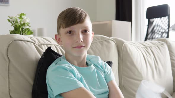 A Young Boy Takes Off a Face Mask and Looks at the Camera As He Sits on a Couch at Home - Closeup alt