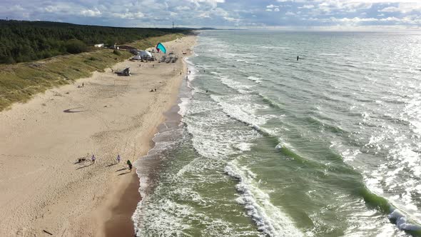 AERIAL: People Walking on a Beach with Surfer Surfing Alongside Baltic Sea Beach alt