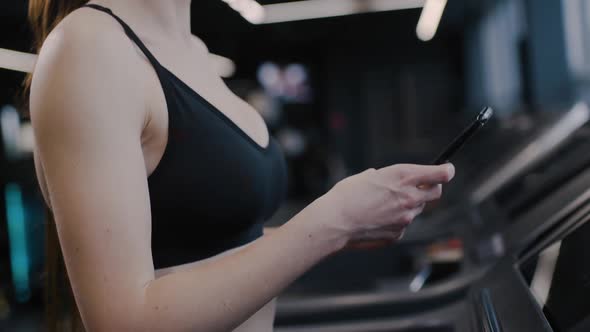 Gym Woman Athlete Walks on a Treadmill and Uses Smartphone Tracking Progress in Sports Aerobic alt