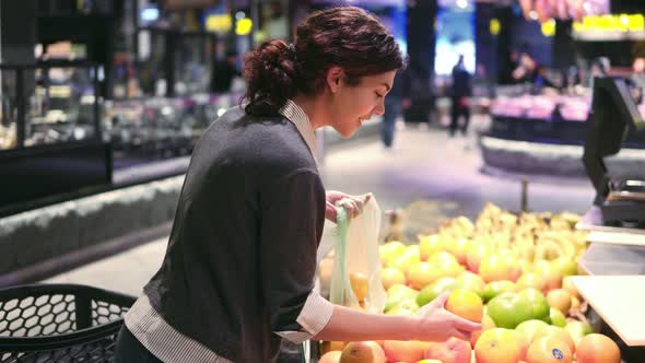 Young Beautiful Brunette Girl in Her 20's Picking Out Oranges Into a Plastic Bag at the Fruit and alt