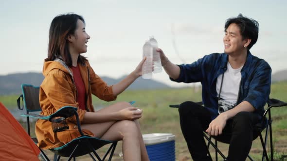 Asian couple drinking water after setting up a camping tent enjoy the vacation time.