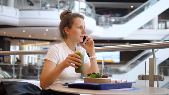 Lunch Break of a Businesswoman. Young Woman Talking on the Phone, Smiling and Drinking Her Green alt