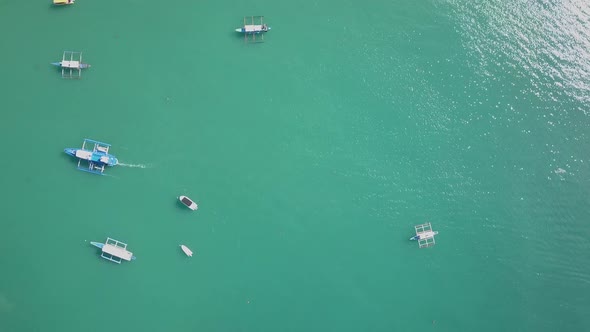 Aerial view directly down on emerald green waters with traditional filipino boats tracking shot to E alt