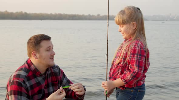 Father Showing Fish Bait To Daughter Near Lake