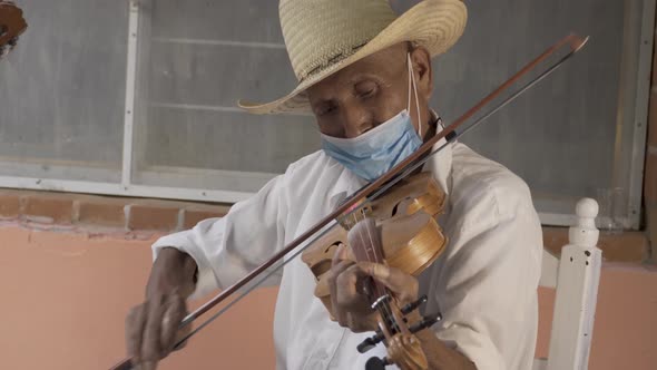 Closeup shot of a Hispanic aged musician with a hat and a mask playing violin on the street alt