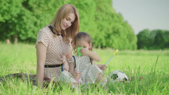 Joyful Young Mother Helping Cute Little Girl To Blow Soap Bubbles. Portrait of Cheerful Happy alt