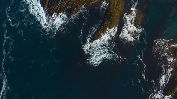 Aerial view through the clouds of the waves crashing on rocks.