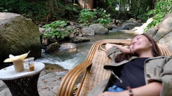 Blurred of a woman lying and relaxing on wooden couch by waterfall stream