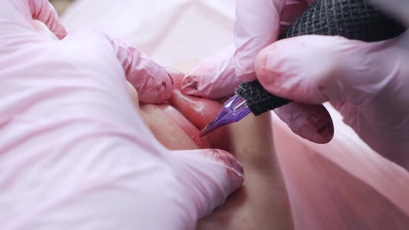 Cosmetologist Applying Pink Pigment Permanent Tattoo on Female Lips with Tatooing Needle Machine at