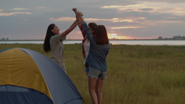 Group of a young Asian women camping pitch a tent while sunset enjoying having fun together.