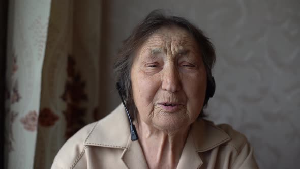 Very Old Woman in Headphones Making Video Conversation in Their Home alt