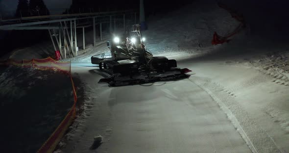Aerial View. Snow Grooming Snowcat Machines Fix Trail on Ski Resort Slope at Night. alt