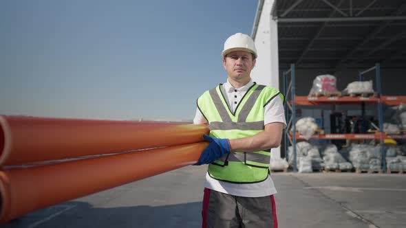 Portrait of Confident Serious Caucasian Man in Hard Hat and Uniform Walking Holding Pipes alt
