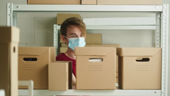 Man Wearing Medical Face Mask and Protective Gloves Taking Parcel From Shelf Employee of Warehouse alt