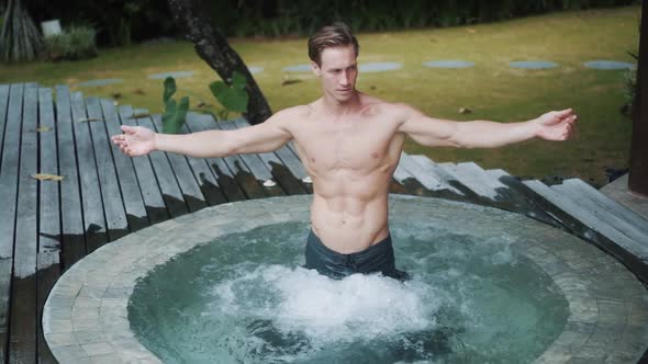 Sexy Guy with Sporty Body Stands in Jacuzzi and Opens His Arms Wide Slow Motion alt