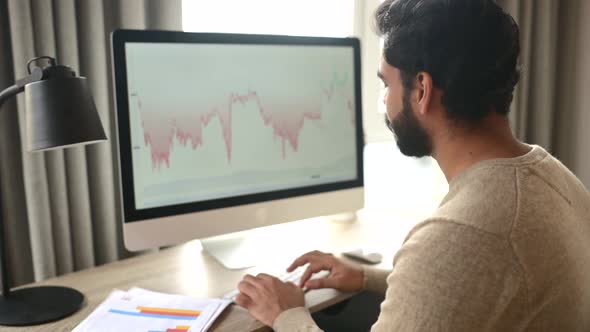 Indian Male Trader Using Computer for Remote Work Making Cryptocurrency Financial Market Analysis