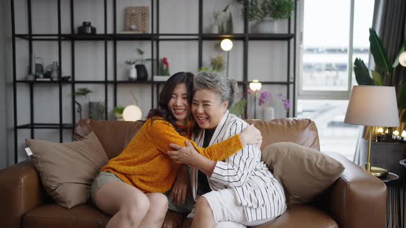 Portrait Asian mature mother and young daughter cuddling in sofa living room at home. alt