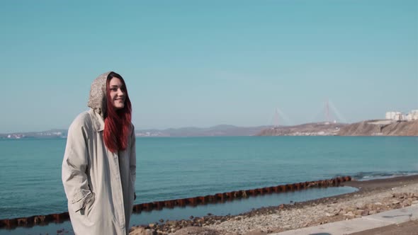 one girl in a coat stands on the shore of a calm sea