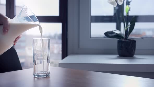 Closeup of a Woman Hand Pouring Milk From a Jug Into a Glass Indoors Cinematic Shot