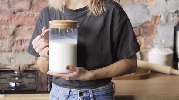 Blonde in Tshirt and Denim Jeans Holds Container with Milk