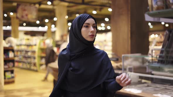 Woman in Hijab Takes Pile of Products From the Shelf in the Supermarket alt